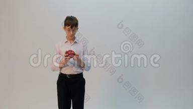 <strong>一个</strong>穿着白色衬衫的年轻人手里扭着<strong>一个红苹果</strong>。 戴眼镜的青少年检查成熟的水果。 复制空间。 这就是